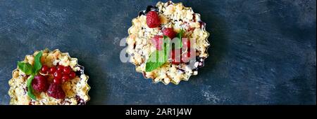 Portionsbeere zerbröckelt in einer Backform auf dunklem Hintergrund. Beerentartlets mit Mürbeteig und saftiger Füllung. Leichte Sommerdessert. Stockfoto