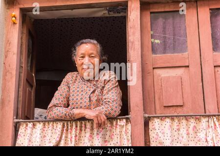 Freundliche, hochrangige nepalesische Frau im Fenster ihres Hauses in Kirtipur, Nepal Stockfoto