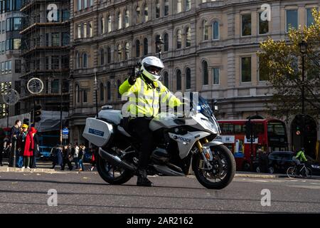 London, GROSSBRITANNIEN - 11. November 2019: Der britische Polizeibeamte auf dem Motorrad stoppt den Autoverkehr an der belebten trafalgar Square Kreuzung für den staatlichen esc Stockfoto