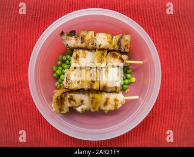 Über Kopf Schuss von Schweinefleisch auf Spieße mit grünen Bohnen in Eine Kunststoffschale auf einer roten Oberfläche Stockfoto