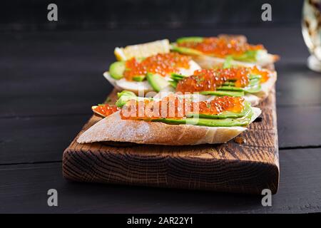 Sandwiches mit lachsrotem Kaviar mit in Scheiben geschnittenem Avocado. Sandwich zum Mittagessen. Hochwertige Lebensmittel. Stockfoto