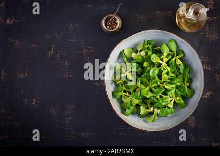 Frische Blätter von Maissalat in einer Schüssel auf dunklem Hintergrund. Vegetarische/vegane Küche. Diätetische Speisen. Stockfoto