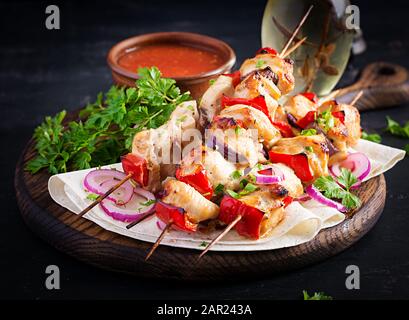 Gegrilltes Hühnerkebab mit Paprika auf einem Holzbrett. Gegrillte Fleischspieße, schischiger Kebab auf dunklem Hintergrund. Stockfoto