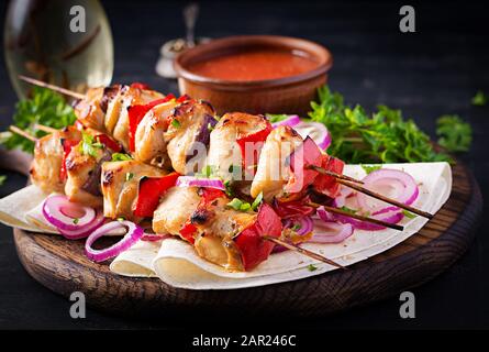 Gegrilltes Hühnerkebab mit Paprika auf einem Holzbrett. Gegrillte Fleischspieße, schischiger Kebab auf dunklem Hintergrund. Stockfoto