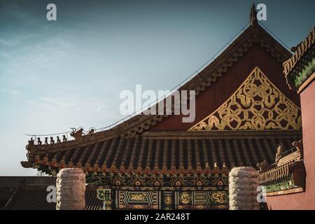 Traditionelles chinesisches Pagodendach in der Verbotenen Stadt Peking. Goldenes und rotes Design in blauem Himmel als Hintergrund. Stockfoto