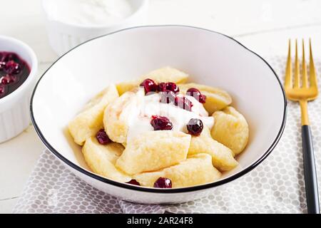 Traditionelle ukrainische / russische Hüttenkäse faule Knödel serviert mit saurer Sahne und Kirschmarmelade auf weißem Holzhintergrund. Stockfoto