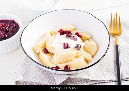Traditionelle ukrainische / russische Hüttenkäse faule Knödel serviert mit saurer Sahne und Kirschmarmelade auf weißem Holzhintergrund. Stockfoto