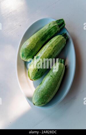 Baby Zucchini auf weißem Plattenhintergrund über weißem Holztisch. Organische Lebensmittel. Stockfoto