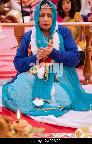 Ein Hindu devotee feiert ihren 70. Geburtstag durch das Sitzen auf dem Altar und der Unterstützung in der Morgen. In Jamaica, Queens, New York City. Stockfoto