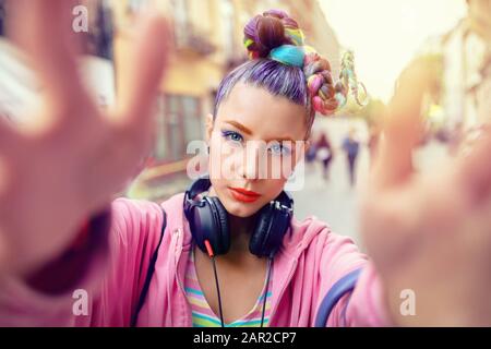 Verspieltes cooles hippy junges Mädchen mit Kopfhörern und verrückten Haaren, die selfie auf der Straße einnehmen Stockfoto