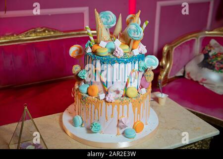 Bunte Kuchen in Waffelkegel für Eis im Sortiment, mit Süßwaren bestreut auf weißem Holztisch. Blauer Kuchen mit Farbtönen Stockfoto