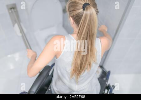 Die junge Frau, die im Rollstuhl sitzt, greift die Handläufe für Behinderte. Konzept für Barrierefreiheit. Stockfoto