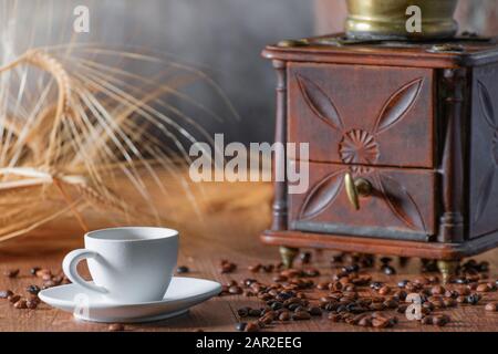 Nahaufnahme einer Tasse Kaffee mit gerösteten Kaffeebohnen und einer alten Mühle auf einem Holztisch. Entspannungskonzept. Stockfoto