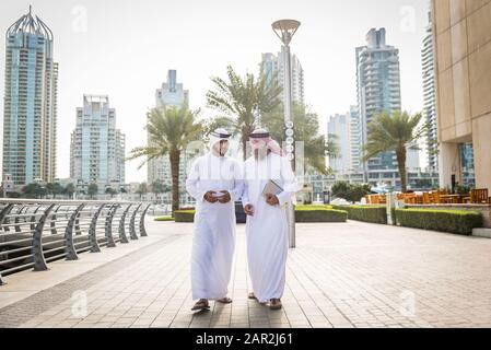 Zwei Geschäftsleute mit traditioneller emirates-kleidung treffen sich in Dubai - ältere und junge Erwachsene, die in den Vereinigten Arabischen Emiraten geschäftlich tätig sind Stockfoto