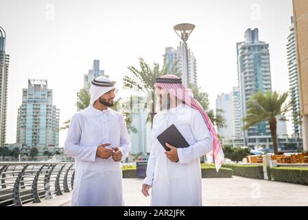 Zwei Geschäftsleute mit traditioneller emirates-kleidung treffen sich in Dubai - ältere und junge Erwachsene, die in den Vereinigten Arabischen Emiraten geschäftlich tätig sind Stockfoto