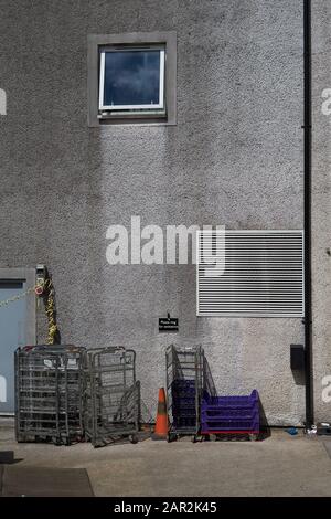 Außenwand des Industriegebäudes mit verschiedenen kommerziellen Wagen, Fenster, Lüftungsschlitz und Hinweisschild "Bitte um Hilfe rufen" Stockfoto