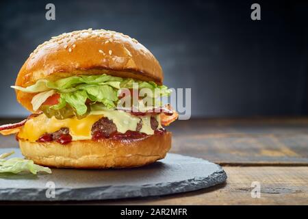 Großer Hamburger auf schwarzem Schieferteller über dunklem Hintergrund. Kopierbereich Stockfoto