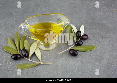 Olivenöl aus Glas mit schwarzen Oliven und Blättern auf rustikalem Hintergrund Stockfoto