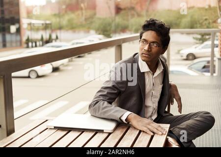 Junge schöne Indische Mann in einem weißen Hemd und Anzug sitzt Stockfoto