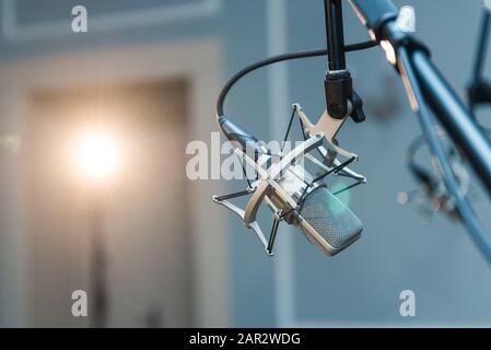 Ein professionelles silbernes Kondensatormikrofon, das auf einem schwarzen Stativ montiert ist und in einem Konzertsaal mit Punktbeleuchtung aufgestellt ist. Stockfoto