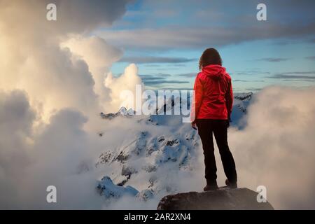 Abenteuerliches Mädchen, das den Wunderschönen Dramatischen Sonnenuntergang über den Bergen beobachtet. Verbundbild mit Landschaftsaufnahme in British Columbia, Kanada. Kon Stockfoto