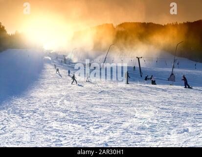 Skigebiet, Snowmaking auf künstlichen Pisten bei Sonnenuntergang. Skifahrer und Snowboarder auf der Piste. Stockfoto