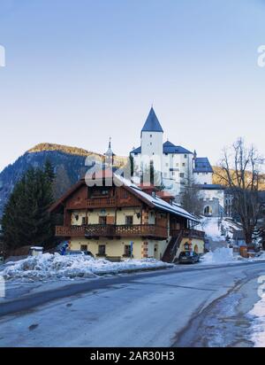 MAUTERNDORF, Salzburger Lungau, ÖSTERREICH, 21. JANUAR 2020: Schloss in Mauterndorf mit einem traditionellen Holzhaus im Vordergrund im Winter. Vertikal Stockfoto