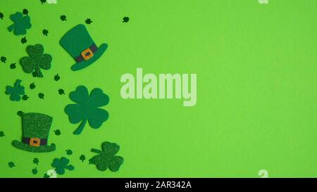 Happy St. Patrick's Day Banner-Design. Shamrockblättchen in Draufsicht und Hüte der irischen Elf auf grünem Hintergrund. Saint Patricks Day Flat Lay Komposition Stockfoto