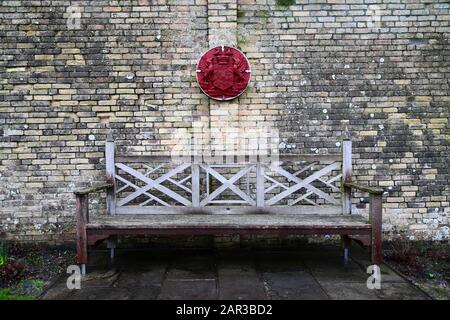 Holzbank und Wappen des Earl of Dunraven an der Wand in Gärten, die einst Teil des Anwesen Dunraven Castle, South Glamorgan, Wales, Großbritannien waren Stockfoto