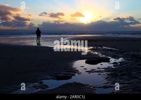 Person, die bei Sonnenuntergang am Strand in der Dunraven Bay in der Nähe von Southerndown, South Glamorgan, Wales, Großbritannien spaziert Stockfoto