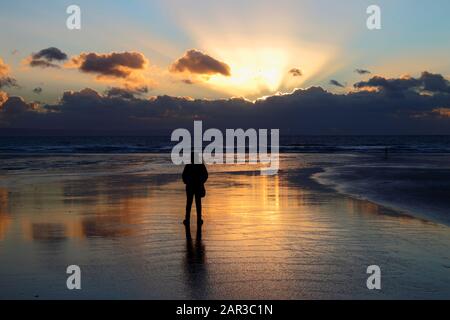 Person am Strand in Dunraven Bay mit Blick auf den Sonnenuntergang, in der Nähe von Southerndown, South Glamorgan, Wales, Großbritannien Stockfoto