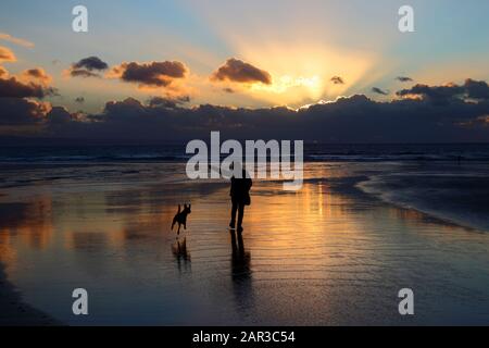 Person, die bei Sonnenuntergang am Strand in der Dunraven Bay in der Nähe von Southerndown, South Glamorgan, Wales, Großbritannien spaziert Stockfoto