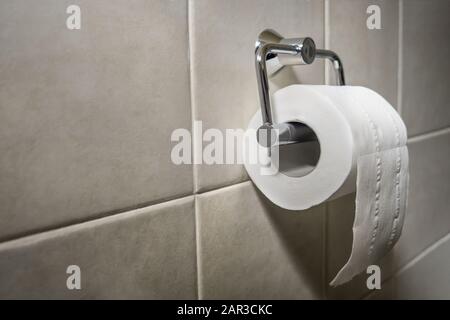 Rolle von toilettenpapier auf Metallpapierhalter. Badezimmergewebe an der Wand. Toilettenpapier. Weiches weißes toilettenpapier auf gefliestem Hintergrund. Hintergrund mit weißen Kacheln Stockfoto