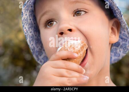 Vier fünf Jahre altes Kind, Junge, der Eis isst. Kleiner Junge, der Dessert isst. Eis in der Hand des Kindes. Kind mit Eiscreme im Kegel, Nahaufnahme. Junge isst Eis Stockfoto