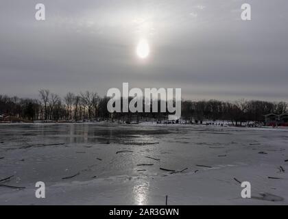 Sonne bedeckt von Wolken Sonnenlicht reflektiert auf dem Eisschild eines Sees im mont-royal-Park in quebec im Winter 2020 Stockfoto