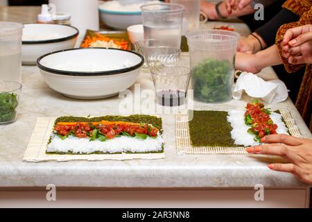 Studenten an einem Küchenschalter lernen, wie man Sushi-Rollen in einer Klasse macht Stockfoto