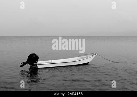 Graustufenaufnahme eines leeren Motorbootes auf der Ruhe Oberfläche des Wassers Stockfoto