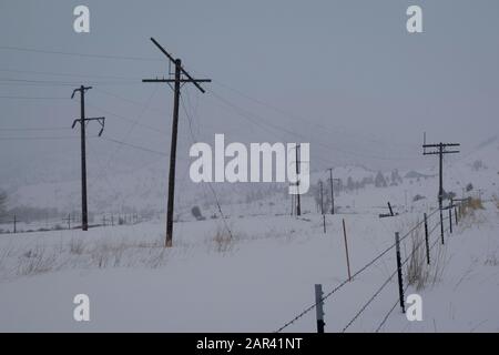 Stromleitungen in den John Long Mountains, in der Nähe von Bearmouth, Montana, und Stacheldrahtzaun während eines Schneesturms. Stockfoto