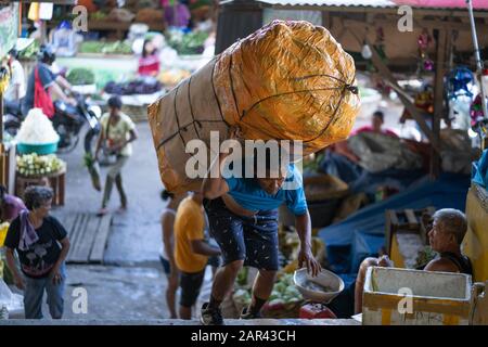 Ein Filipino Mann trägt eine schwere Last von Gemüse auf dem Markt von Cebu City, Philippinen Stockfoto