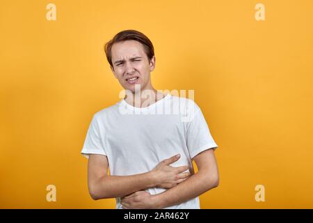 Magenschmerzen Magenprobleme weißes T-Shirt junger Mann auf gelbem Hintergrund. Stockfoto