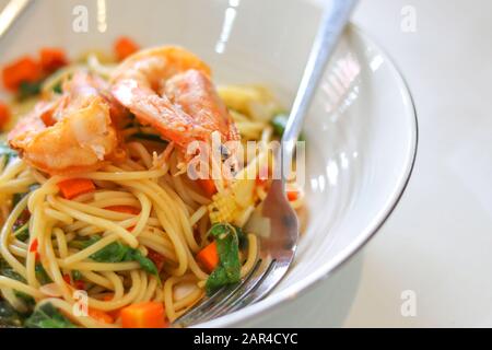 Spaghetti und gebratene Garnelen auf einem weißen Teller mit Gabel. Stockfoto