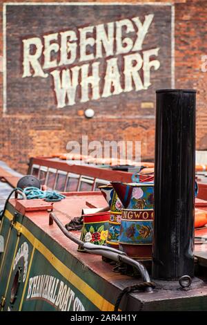 BIRMINGHAM, Großbritannien - 28. MAI 2019: Hell bemaltetes Schmalboot am Kanal am Brindley Place vor der Victorian Regency Wharf mit Schild Stockfoto