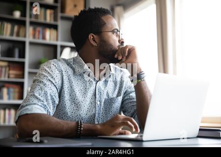 Nachdenklicher, ernster afrikaner sitzt mit Laptop und denkt an das Projekt Stockfoto