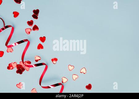 Rotes, herzförmiges Konfetti und Band auf blauem Hintergrund mit Kopierraum. Stockfoto