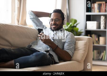 Entspannter afrikaner tragen Kopfhörer Chill auf dem Sofa Hörbuch Stockfoto