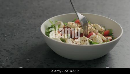 Man handpflücken Salat mit Mozzarella, Kirschtomaten und Friseeblättern in weißer Schüssel auf Terrazzooberfläche, breites Foto Stockfoto