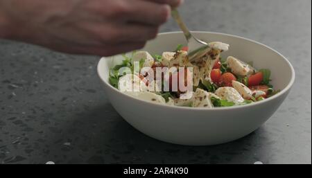 Man handpflücken Salat mit Mozzarella, Kirschtomaten und Friseeblättern in weißer Schüssel auf Terrazzooberfläche, breites Foto Stockfoto