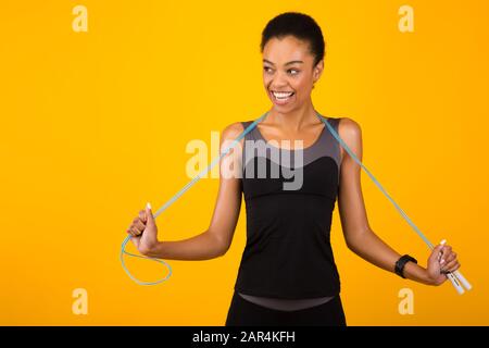 Schwarze Frau mit Springseil, die auf gelbem Studiohintergrund posiert Stockfoto