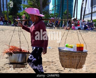 Ein Lebensmittelverkäufer von Frauen trägt zwei Körbe an einem Schulterpol entlang des Strandes in Nha Trang in Vietnam, Asien, Südostasien, an einem heißen, sonnigen Tag während des Tet-Neujahrs. Stockfoto