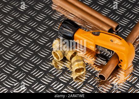 Kupferrohr und Cutter mit Leitungen Stecker auf Stahl Riffelblech Oberfläche. Sanitär Werkzeug und Ersatzteile Stockfoto